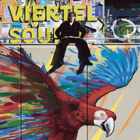 Leo Mazzarella sitzt auf einer Mauer mit einem Graffiti-Papagei